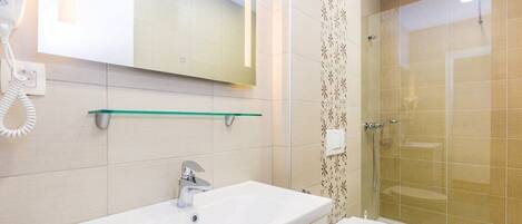 Un bagno con lavandino bianco, uno specchio, box doccia in vetro e un water.