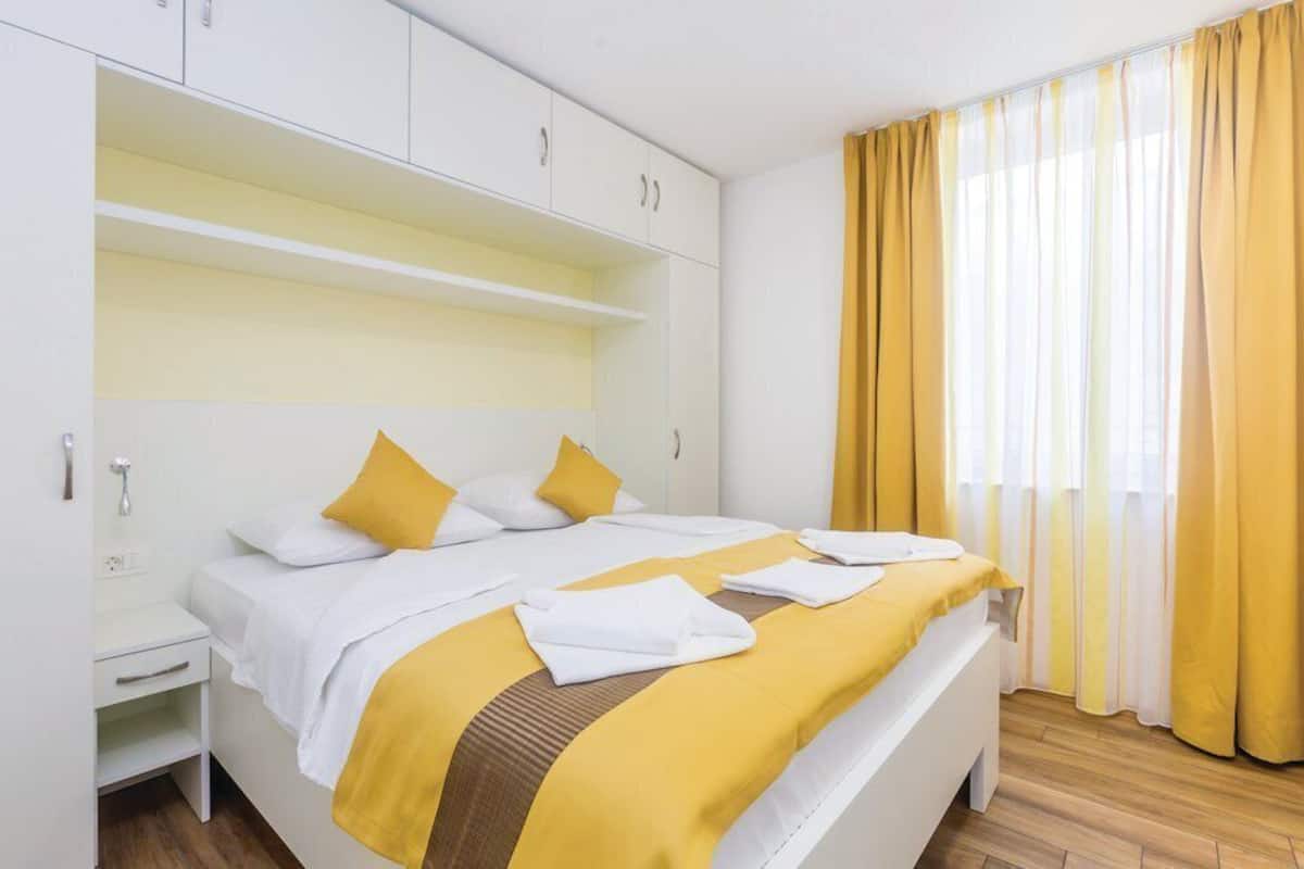 A hotel room with a bed, white wardrobe, and a window with yellow curtains.