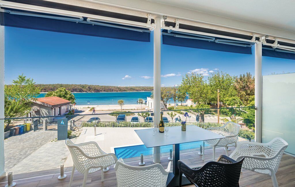 Un balcon avec une table et des chaises, donnant sur une plage et des eaux turquoise.