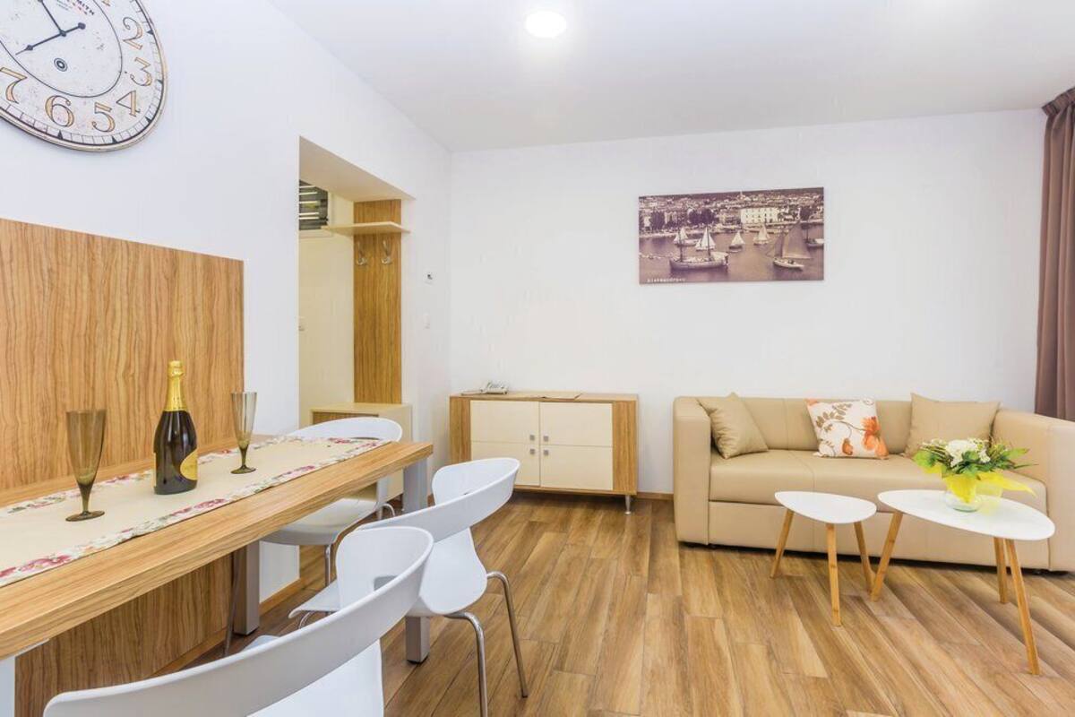 A modern living room with a wooden dining table, white chairs, a beige sofa, and a small white table with a vase.