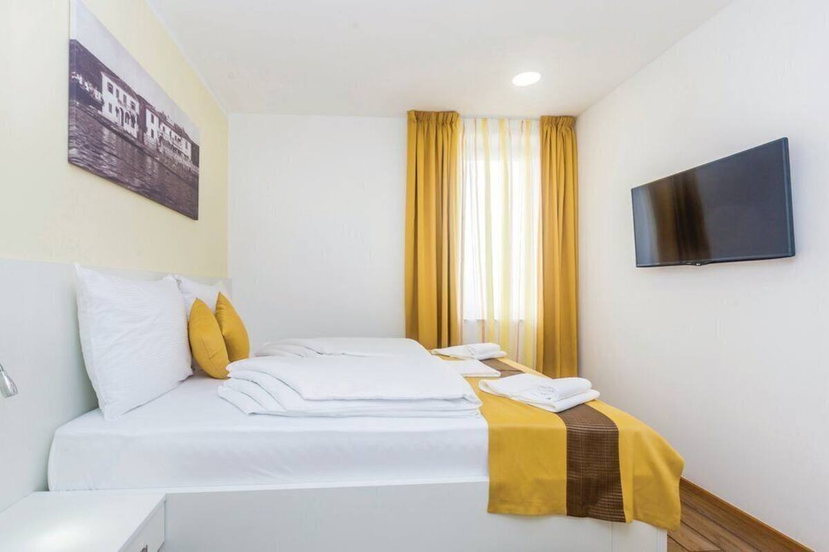 A hotel room with a bed, a flat-screen TV, a painting on the wall, and a window with curtains.