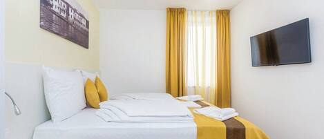 A hotel room with a bed, a flat-screen TV, a painting on the wall, and a window with curtains.