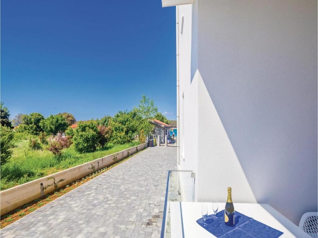 A balcony with a view of a paved path and greenery, a bottle of champagne, and a white wall.