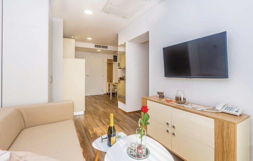 Una sala de estar moderna con un sofá, una mesita con una botella y un florero, y un mueble de madera con un teléfono. Un televisor está montado en la pared.