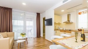 Uma sala de estar moderna com sofá, duas mesinhas, televisão e área de cozinha com mesa de jantar para dois.