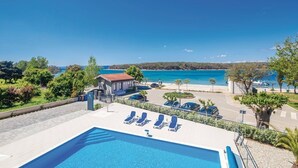Área de piscina com espreguiçadeiras, um pequeno edifício e vista para o mar.