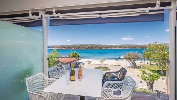 Varanda com mesa e cadeiras, com vista para a praia e o mar.