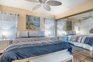 A bedroom with a large bed, two bedside tables, a mirror, and artwork on the walls. - Sandy Toes @ MP 116 | Pools | Beach Boardwalk (Port Aransas)