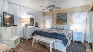A bedroom with a bed, a desk, a chair, a TV, a ceiling fan, and a window with curtains. - Sandy Toes @ MP 116 | Pools | Beach Boardwalk (Port Aransas)