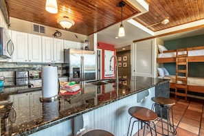 Cozinha moderna com ilha central, eletrodomésticos de aço inoxidável e área de bar com banquetas.