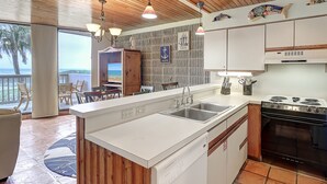 A modern kitchen with a large island, stainless steel appliances, and a view to the outdoors. - Surf-Shells-Sandcastles | Ocean-Pool Views | MP214 (Port Aransas)