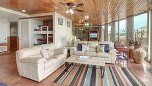 A spacious living area with a wooden ceiling, a ceiling fan, a beige sofa, a coffee table, and a large window offering a view. - Surf-Shells-Sandcastles | Ocean-Pool Views | MP214 (Port Aransas)