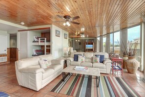 A spacious living area with a wooden ceiling, a ceiling fan, a beige sofa, a coffee table, and a large window offering a view. - Surf-Shells-Sandcastles | Ocean-Pool Views | MP214 (Port Aransas)