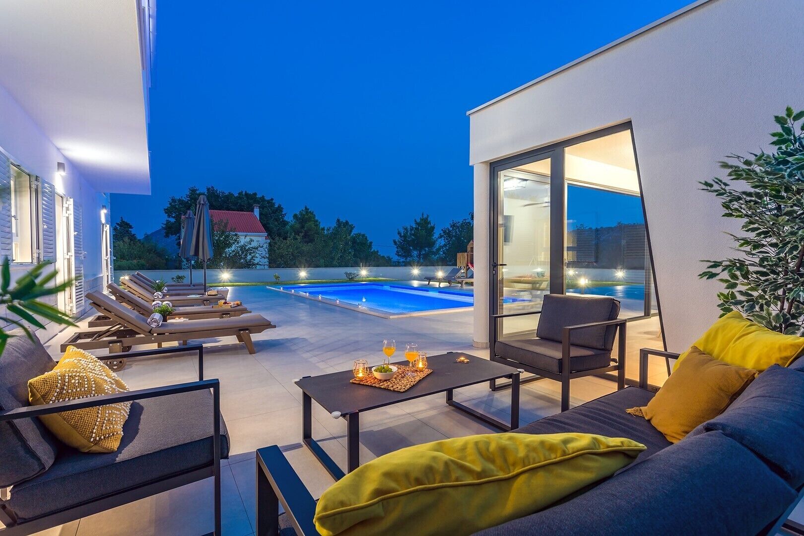 A modern outdoor living area with a pool, lounge chairs, and a dining table with cushions.