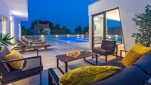 A modern outdoor living area with a pool, lounge chairs, and a dining table with cushions. - VILLA ALMIC with heated pool, 5 bedrooms, Media room,multi-use playground court (Naklice)