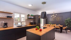 A modern kitchen with a central island, black cabinets, wooden countertops, and a dining area with a table and chairs. - VILLA ALMIC with heated pool, 5 bedrooms, Media room,multi-use playground court (Naklice)