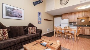Een woonkamer met een bruine bank, een salontafel en een eethoek met houten stoelen en een tafel.