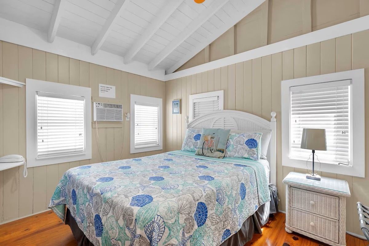 A bedroom with a bed, a nightstand, and a window with blinds.