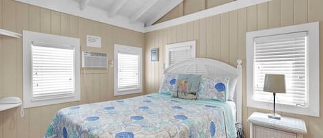 A bedroom with a bed, a nightstand, and a window with blinds.