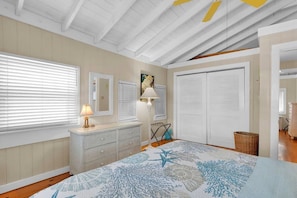 A bedroom with a bed, dresser, and two windows with blinds.