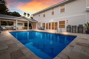 A swimming pool with a stone deck, a covered patio area, and a white building with large windows and a door.