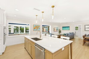 A modern kitchen with a central island, stainless steel appliances, and pendant lighting. - Take Me Away - Stylish Coastal Escape with Pool Near Beach and Trolley (Holmes Beach)