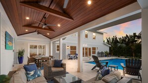 An outdoor patio with wicker furniture, a pool, and a view of a house. - Take Me Away - Stylish Coastal Escape with Pool Near Beach and Trolley (Holmes Beach)