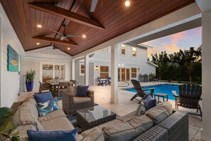 An outdoor patio with wicker furniture, a pool, and a view of a house.