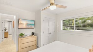 A bedroom with a bed, a ceiling fan, a TV on the wall, and a window with blinds.