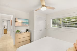 A bedroom with a bed, a ceiling fan, a TV on the wall, and a window with blinds.