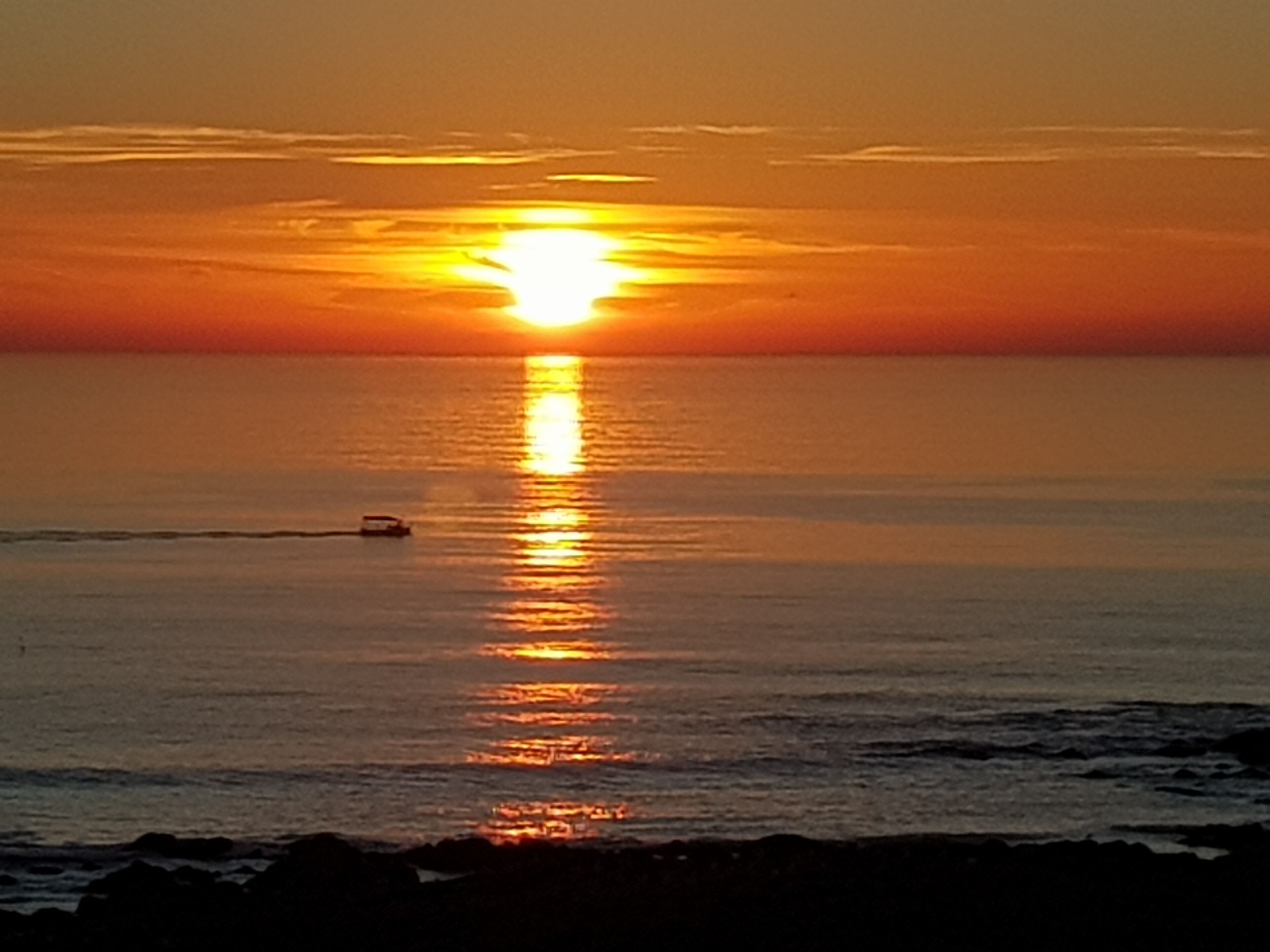A sunset over a calm sea with a boat in the distance.