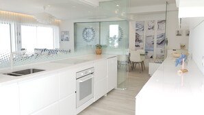 A modern kitchen with a large island, white cabinetry, and a glass partition. - Blue Beach Apartment (Póvoa de Varzim)