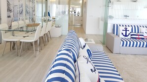 A modern living room with a glass dining table, white chairs, a striped sofa, and nautical-themed decor. - Blue Beach Apartment (Póvoa de Varzim)