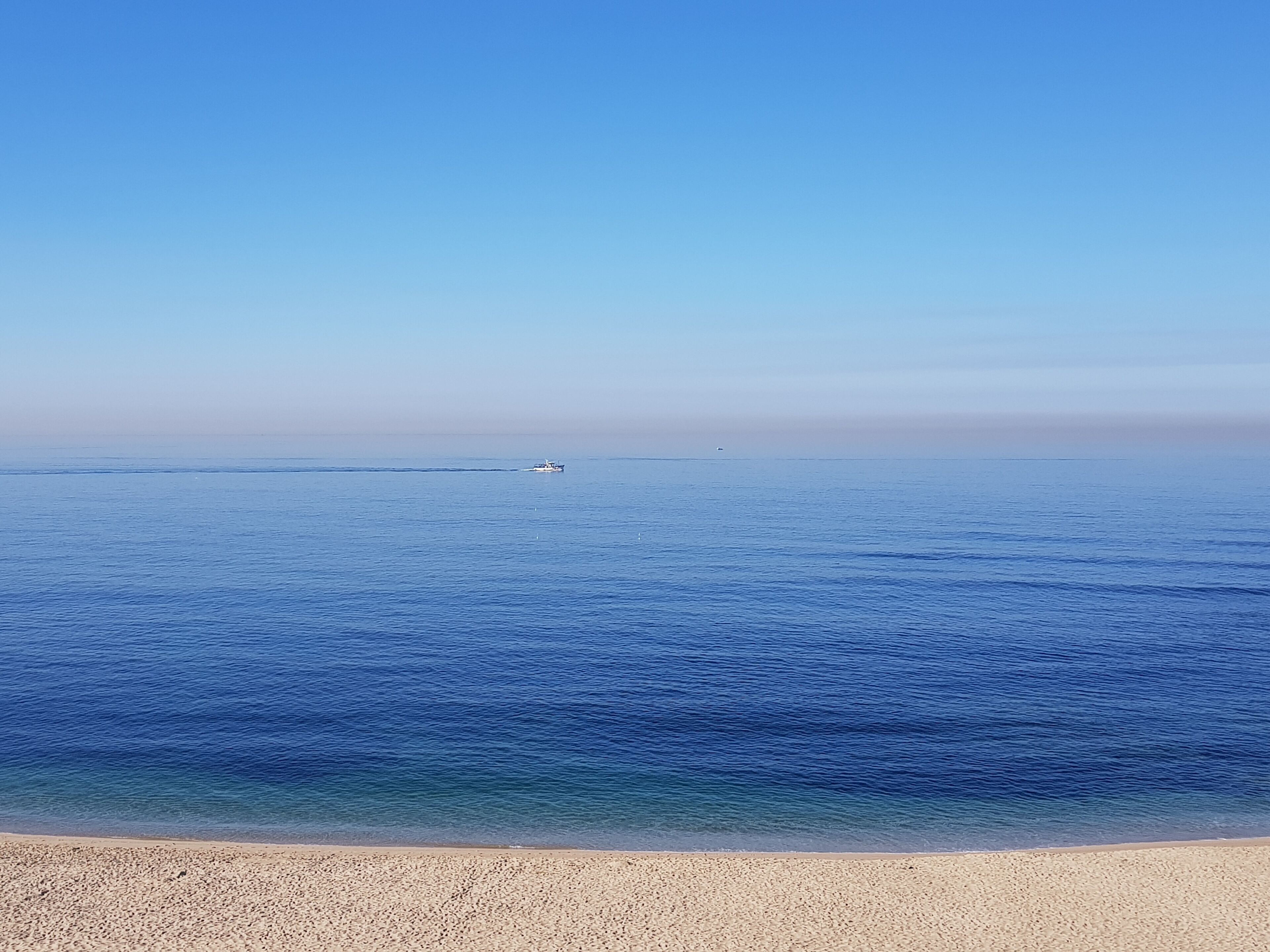 Une plage avec une eau d’un bleu limpide et un bateau qui se trouve au loin.