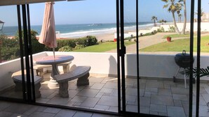 A balcony with a view of the ocean, a grill, and a seating area with a table and chairs.