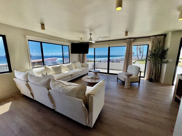 A spacious living room with a large white sofa, a coffee table, and a TV mounted on the wall. - Luxury Ocean view beach villa for 6 guests (Rosarito)