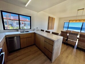 Una cocina moderna con una isla grande, armarios de madera, lavavajillas y vistas al océano.