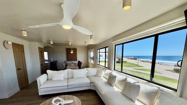 A modern living room with a large sectional sofa, a ceiling fan, and a view of the ocean.