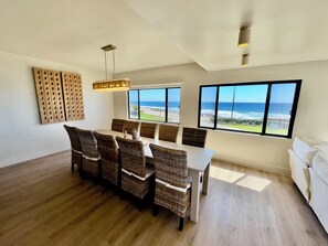 Ein Essbereich mit Korbstühlen, einem weißen Tisch und großen Fenstern mit Meerblick.