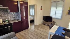 A modern kitchen with dark cabinets, a built-in oven, and a tiled backsplash. There is a dining area with a table, chairs, and a TV. The room has wooden flooring and a ceiling light fixture. - 2 ROOMS GREAT TERRACE ROOFTOP FULL CITY CENTER (Nice)