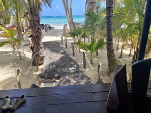 A wooden deck with a pair of shoes, leading to a sandy beach with palm trees and a view of the ocean. - Little Corn Beach and Bungalow (Corn Islands)