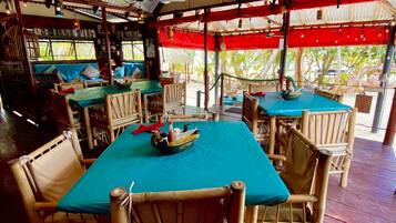An outdoor restaurant with wooden tables and chairs, covered by a red canopy, and a view of the outdoors.