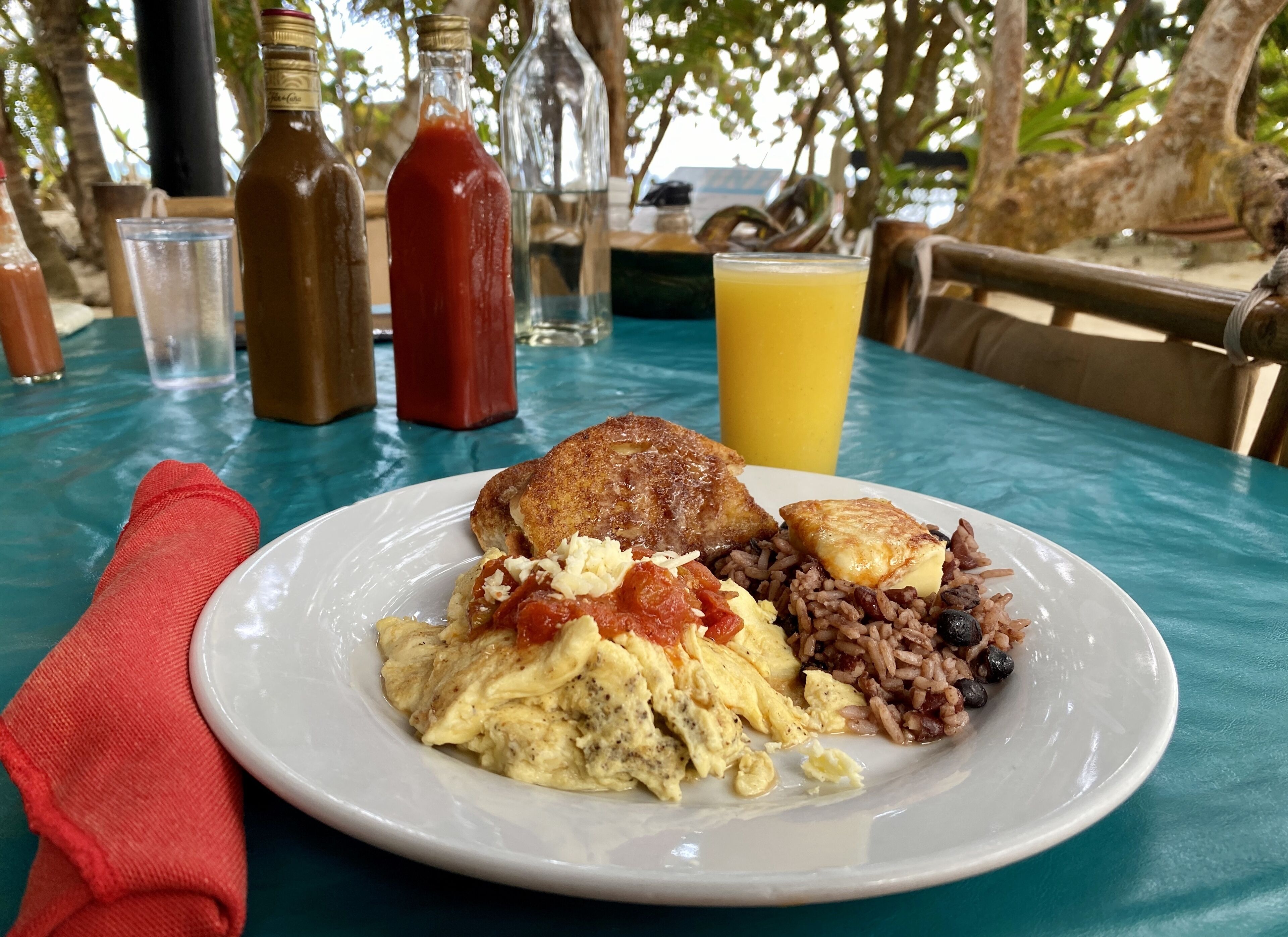 A plate of breakfast food including eggs, beans, and toast, with drinks and a red napkin on a table.