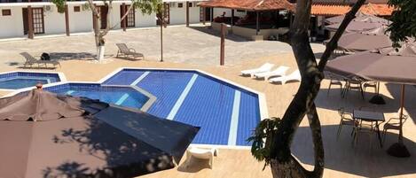 A pool area with lounge chairs and umbrellas, surrounded by buildings with red-tiled roofs.