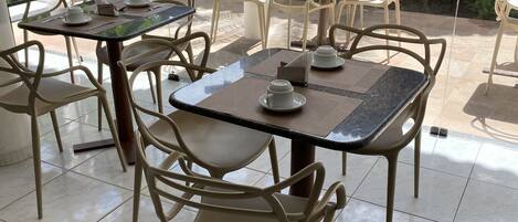 Un restaurante con terraza, mesas y sillas, y vistas al entorno verde.