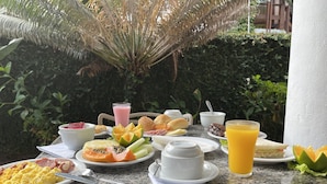 A breakfast table with various dishes, including eggs, toast, and fruit, set outdoors with a view of greenery and a palm tree. - Rede Andrade Estrela Dalva Praia Hotel (Porto Seguro)