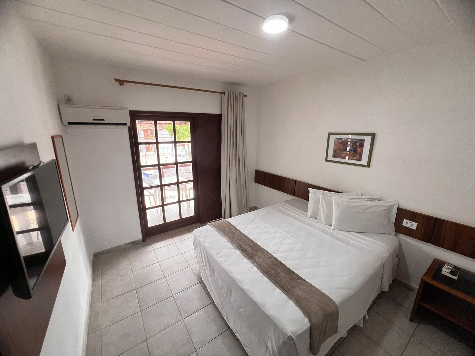 Een hotelkamer met een bed, een televisie, een raam met gordijnen en een deur naar een buitenruimte.