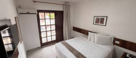 Een hotelkamer met een bed, een televisie, een raam met gordijnen en een deur naar een buitenruimte.