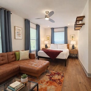 A modern hotel room with a bed, a sofa, a coffee table, and a ceiling fan.