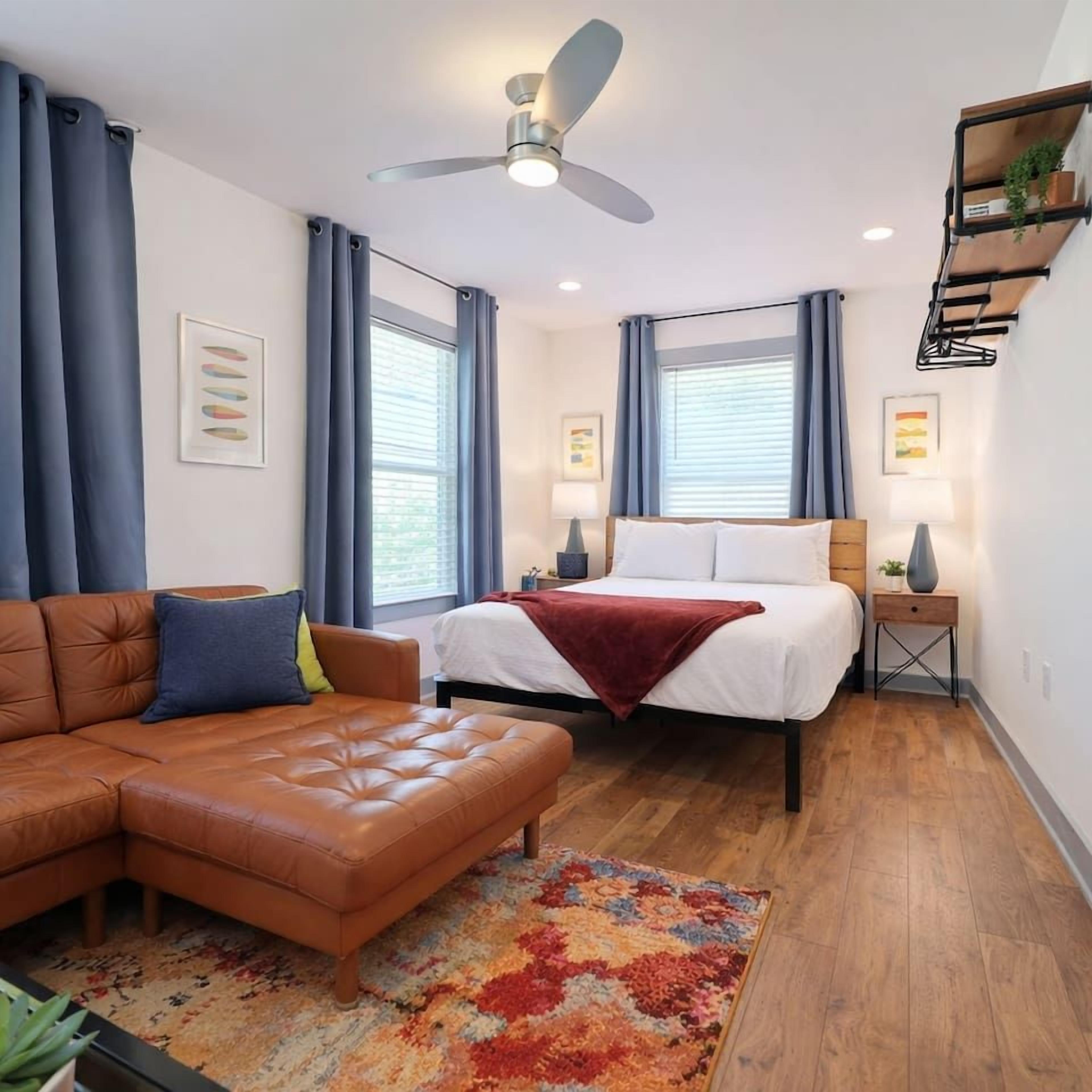 A modern hotel room with a bed, a sofa, a ceiling fan, and a small side table.